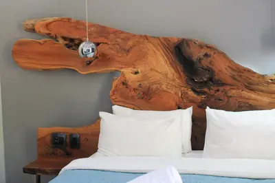 a bed with a wooden headboard with a log on the wall at Nelspruit Lodge in Nelspruit