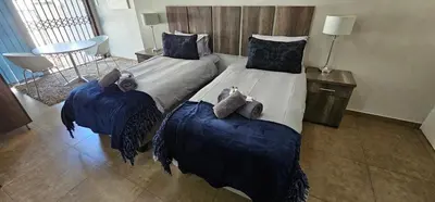 a bedroom with two beds with blue covers and a table at Blue Sparrow Guest House in Middelburg