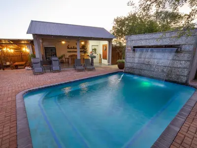 a swimming pool with chairs and a house at The Belgium Inn in Hoedspruit
