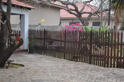a wooden fence in front of a house with pink flowers at Komati Friends in Komatipoort