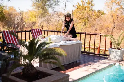a woman is sitting on a bed next to a pool at Mawusi Bush Lodge in Hoedspruit