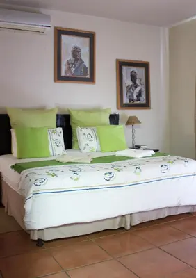 a bedroom with a large bed with green and white pillows at Villa Too Kruger Lodge in Komatipoort
