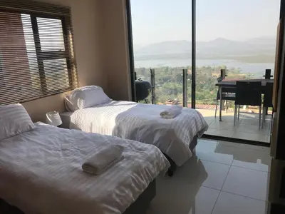 two beds in a room with a large window at Thatch View in Hartbeespoort