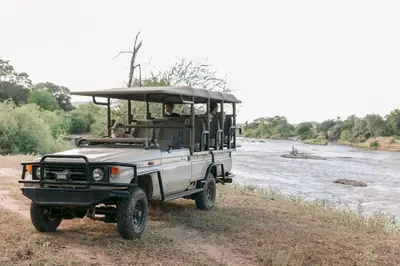 a safari vehicle with people in it on a river at Limpokwena Nature Reserve in Tokio