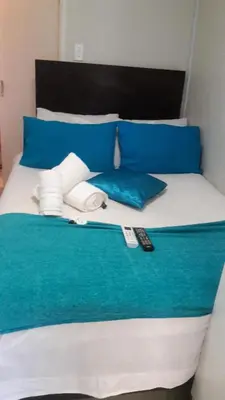 a bed with blue and white pillows and a remote control at Valley Guest House in Pretoria