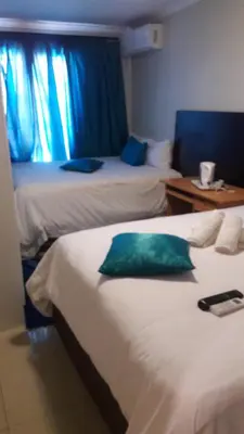 two beds in a hotel room with blue curtains at Valley Guest House in Pretoria