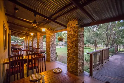 a restaurant with tables and chairs on a wooden deck at Hamiltons Lodge & Restaurant in Malelane