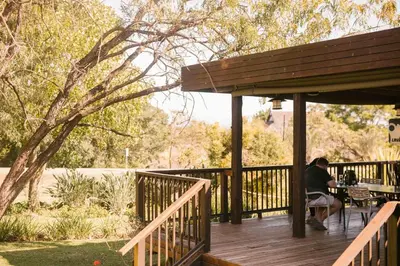 a man sitting at a table on a wooden deck at Hamiltons Lodge & Restaurant in Malelane