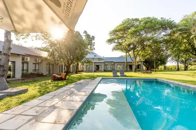 a swimming pool in front of a house with a yard at Hamiltons Lodge & Restaurant in Malelane