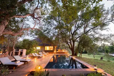 a backyard with a pool with chairs and a wooden deck at Rukiya Safari Camp in Hoedspruit