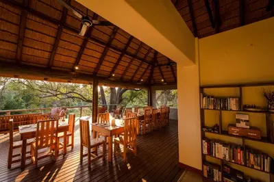 a library with tables and chairs and a book shelf at Rukiya Safari Camp in Hoedspruit