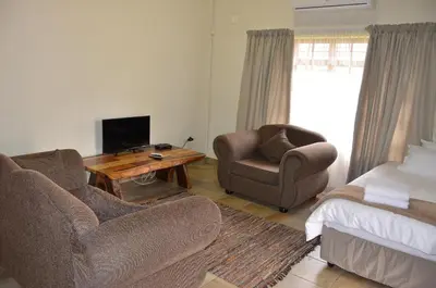 a living room with two chairs and a television and a bed at Stoep At Steenbok Self Catering in Komatipoort