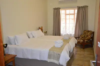 a bedroom with a bed and a chair and a window at Stoep At Steenbok Self Catering in Komatipoort