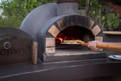 a person is putting a pizza into an oven at The Baobab Bush Lodge and Villa in Hoedspruit