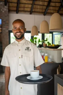 a man holding a tray with a coffee cup on it at The Baobab Bush Lodge and Villa in Hoedspruit