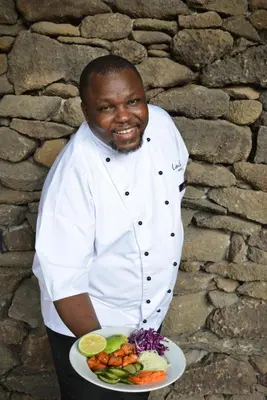a man in a chef uniform holding a plate of food at Lion Sands Narina Lodge in Sabi Sand Game Reserve