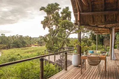 a deck with a table and chairs and a view of a field at Lion Sands Narina Lodge in Sabi Sand Game Reserve