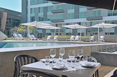 a table with wine glasses on a balcony with a pool at The Capital Menlyn Maine in Pretoria