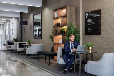 a man sitting in a chair with a laptop in a lobby at The Capital Menlyn Maine in Pretoria