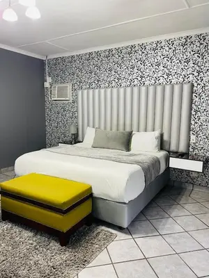 a bedroom with a large bed with a yellow ottoman at Pari Guest House in Middelburg