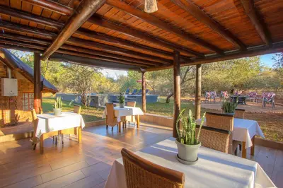 a patio with white tables and chairs and a wooden ceiling at Imbube Safari Lodge in Marloth Park