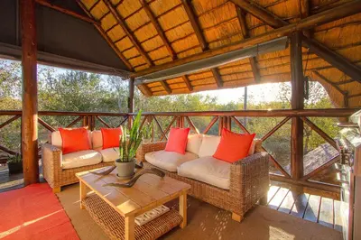 a screened in porch with wicker chairs and a table at Imbube Safari Lodge in Marloth Park
