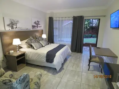 a bedroom with a bed and a desk and a window at Sunbird Garden Cottage in Pretoria