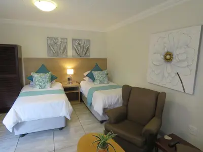 a hotel room with two beds and a chair at Sunbird Garden Cottage in Pretoria