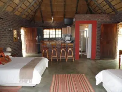 a bedroom with two beds and a kitchen with a bar at Sunset Creek Game Lodge in Karino