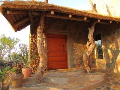a stone house with a wooden door and trees at Kukama's Rest at Zebula 317 in Mabula
