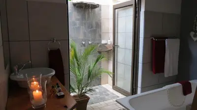 a bathroom with a tub and a shower with a candle at Guinea Feather Country Lodge & Spa in Groblersdal
