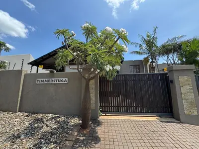 a palm tree in front of a house with a fence at Timmerstuga in Malelane