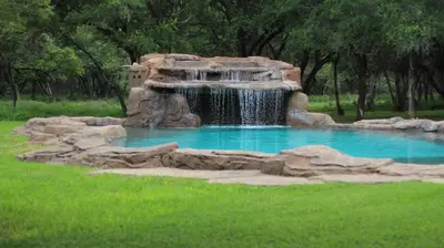 a waterfall in a pool with rocks in a yard at Thabaledi Game Lodge in Brits