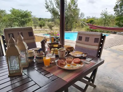 a wooden table with breakfast foods and orange juice at Bushvilla Umoja Kruger in Phalaborwa