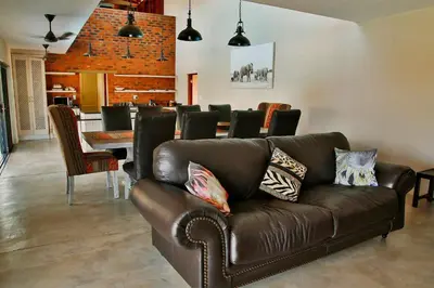 a living room with a leather couch and a dining room at Kierieklapper in Hectorspruit