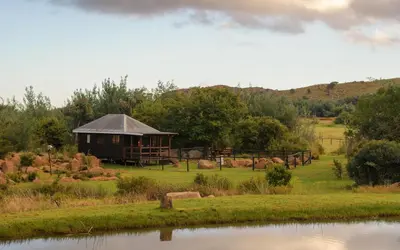a cabin in a field next to a body of water at Riverman Cabin Country Lodge - Tonteldoos in Tonteldoos