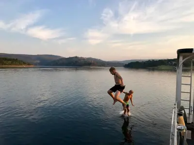 a man and a child jumping off a dock into a lake at Tinkers Lakeside Lodge - Kruger in White River