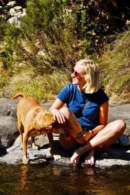 a woman sitting next to a dog in the water at Joy River Backpackers in Moremela