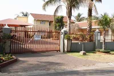 a fence in front of a house with palm trees at Kalahari Guest House in Witbank