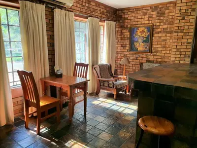 a living room with a table and chairs and windows at Tamboti House in Malelane