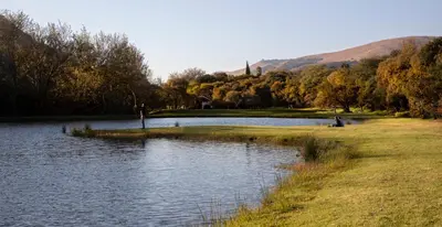 a pond in a park with a person sitting on the grass at Valley of the Rainbow Fly Fishing Estate in Dullstroom