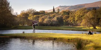 a man with an umbrella standing next to a pond at Valley of the Rainbow Fly Fishing Estate in Dullstroom