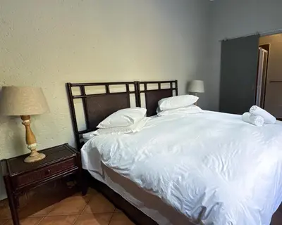 a bedroom with a bed with white sheets and pillows at Paradise Creek Lodge in Malelane