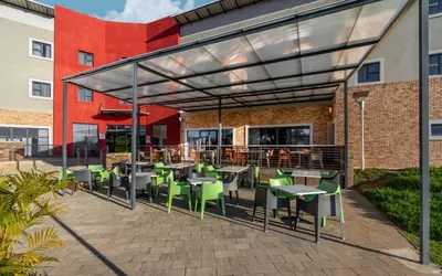 a patio with tables and green chairs and a building at Park Inn by Radisson Polokwane in Polokwane