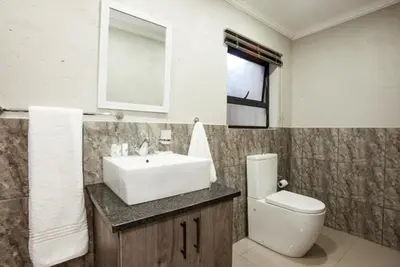 a bathroom with a sink and a toilet and a window at Windmills Rest in Pretoria