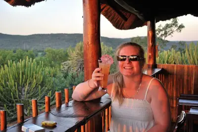 a woman holding up a drink on a porch at River Hill Lodge in Komatipoort