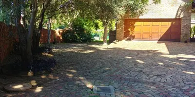 a brick driveway with a garage with a tree at Adorable Designs in Pretoria