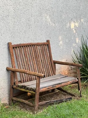 a wooden bench sitting in the grass next to a wall at White Linen Guesthouse in Tierpoort