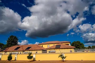 a yellow building with red roofs and a cloudy sky at Hlulani Guest House in Northam
