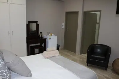 a bedroom with a white bed and a black chair at Hummingbird's Nest in Nelspruit